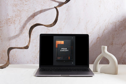 A black laptop sits open on a white tabletop against a textured beige wall, displaying a presentation slide titled 'PEAK CONCEPT'. Decorative elements include a brown wavy metal sculpture on the left and a white ceramic vase on the right.